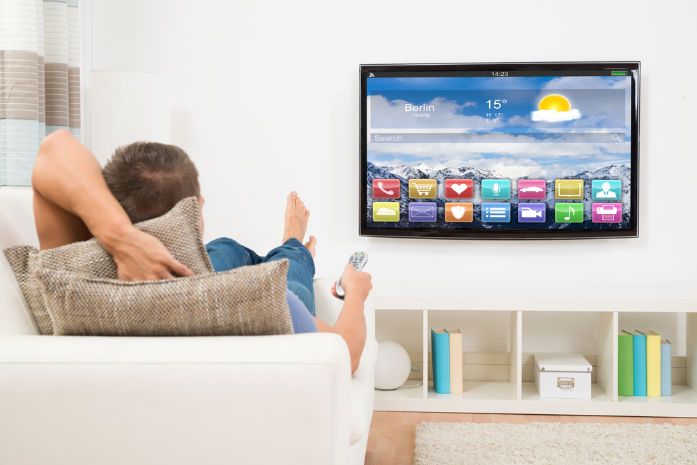 pán leží na gauči a kouká na chytrou televizi
