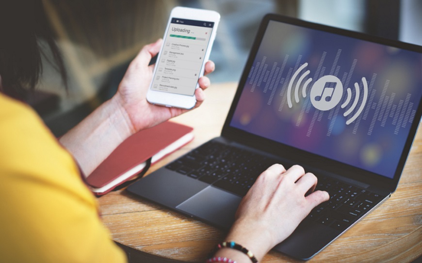 Jak stáhnout hudbu do mobilu (Android i iOS): legální způsoby krok za krokem Žena přesouvá skladby z notebooku do telefonu v kanceláři