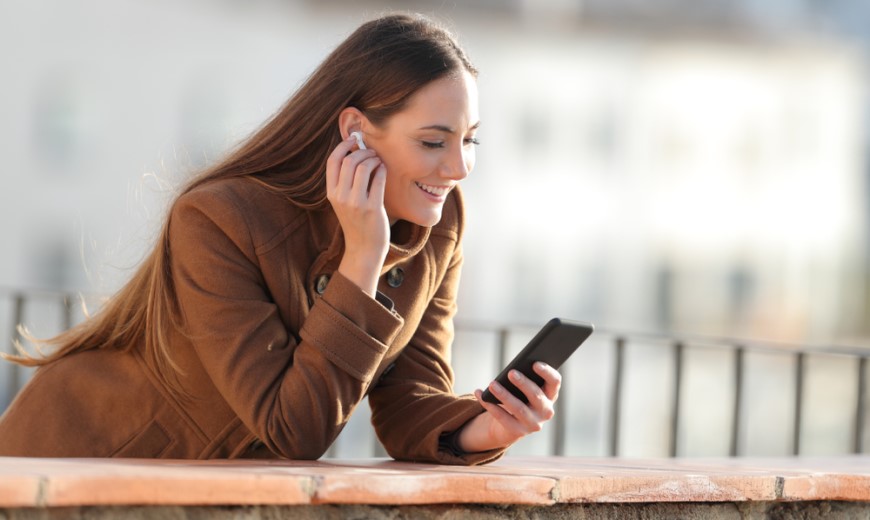 Mladá žena se smartphonem v ruce, která si vkládá bílé sluchátko do ucha