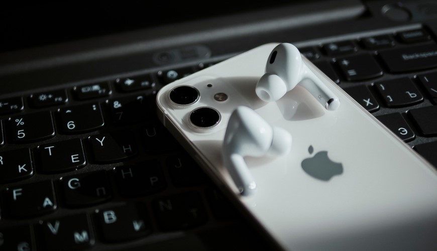 Bezdrátová sluchátka Apple AirPods, odložená na zadní straně iPhonu, který leží na klávesnici notebooku