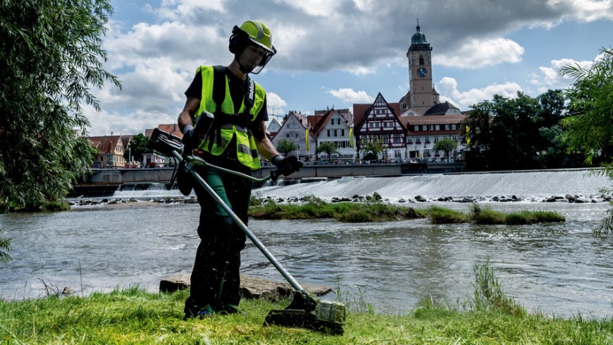 Jak vybrat křovinořez? Muž seká trávu podél řeky pomocí křivonořezu