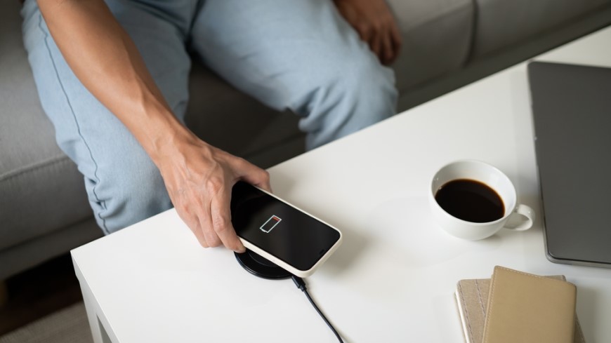 vybitý mobil připojený k powerbance na stolku 