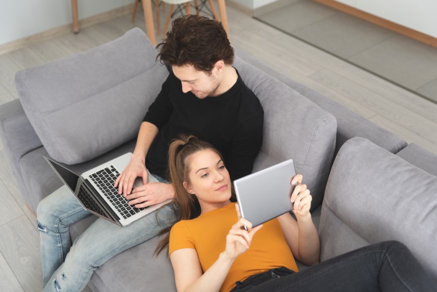 Jak propojit dva routery? Žena si prohlíží videa na tabletu a muž pracuje na MacBooku