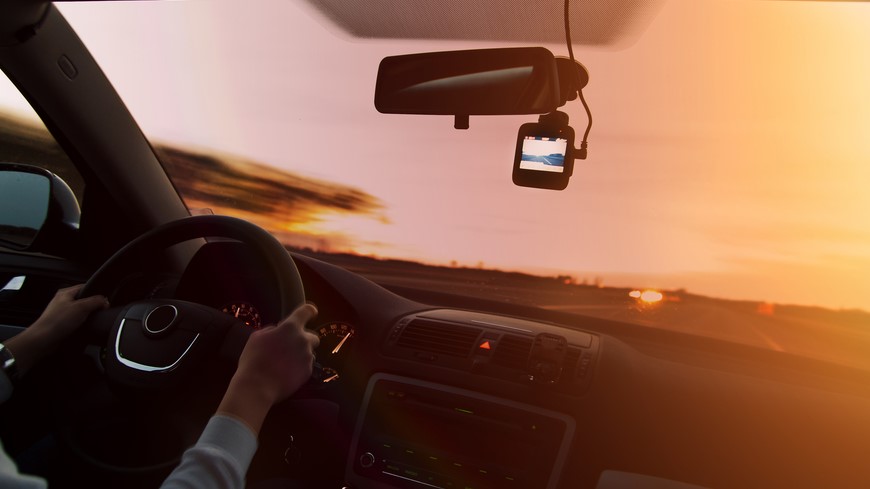 Žena drží volant a jede po silnici. Za zpětným zrcátkem je umístěná autokamera.