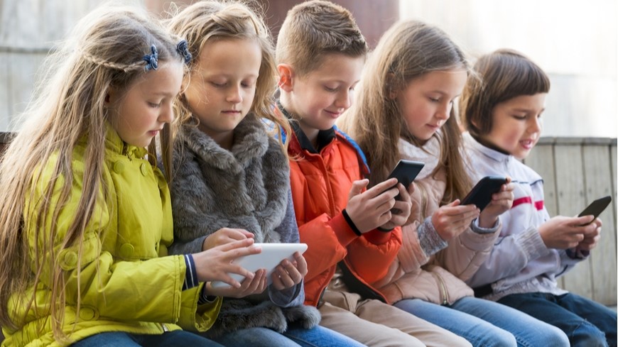 Děti sedí vedle sebe a všechny si hrají na svém mobilním telefonu