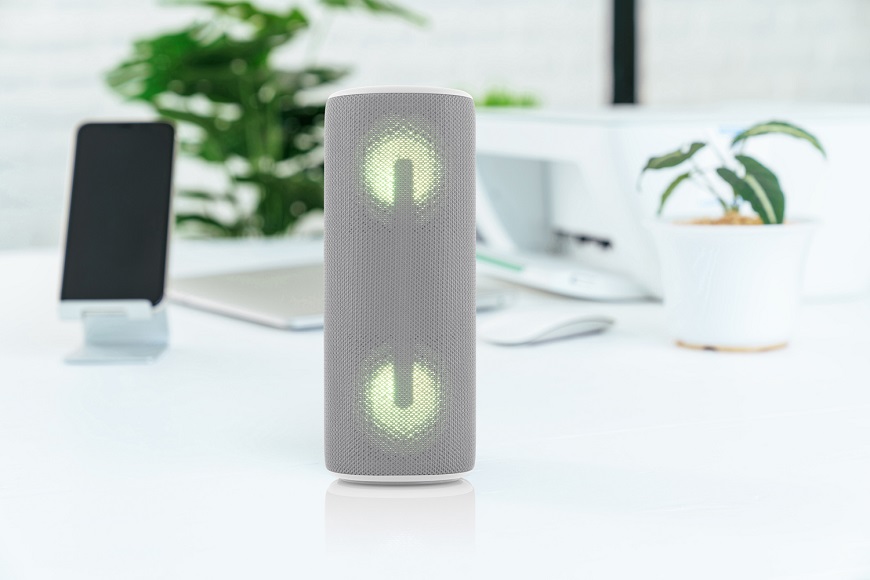 Novinky JVC: Nadupané repro pro každého Šedý přenosný Bluetooth reproduktor JVC XS-E423 se zeleným LED podsvícením na pracovním stole vedle chytrého telefonu