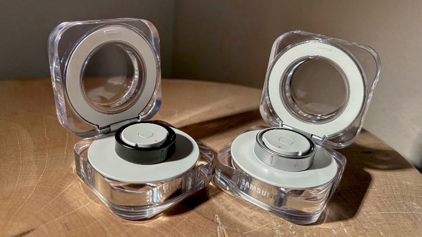 Recenze: Samsung Galaxy Ring – Omotá si vás kolem prstu Chytrý prsten Samsung Galaxy Ring v černém a stříbrném provedení, ležící uvnitř křišťálového nabíjecího pouzdra