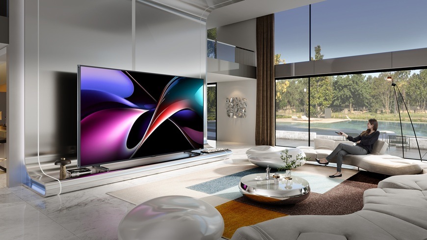 Prémiové televize Hisense přináší luxusní zážitek, který předčí i kino Prémiová televize Hisense 116UXQ z modelové řady 2025 je upevněna na stěně v moderní domácnosti. Paní sedí na gauči a zapíná televizor.