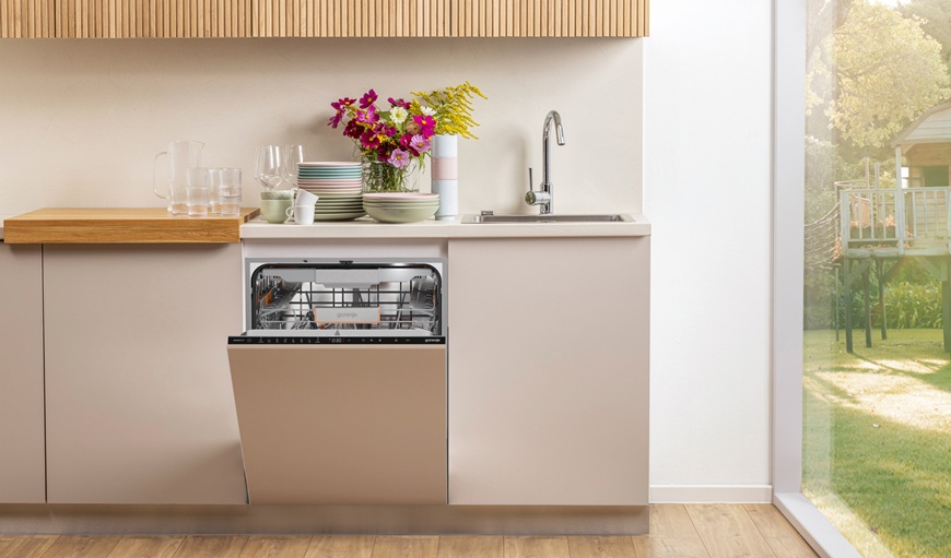 Myčky Gorenje: Funkce Smart Dosing pro efektivní dávkování mycího prostředku Na obrázku je vestavná myčka umístěná v lince. Její dvířka jsou pootevřená. Na pracovní desce je položeno nádobí. Tato myčka disponuje funkcí SmartDosing