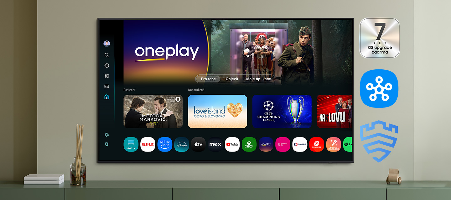 Aplikace na Samsung TV, které posunou vaši televizi na nový level zábavy Domovská strának OS Tizen na obrazovce TV Samsung pověšené na zdi, vpravo loga 7letého plánu upgrade OS zdarma, SmartThings a Samsung Knox