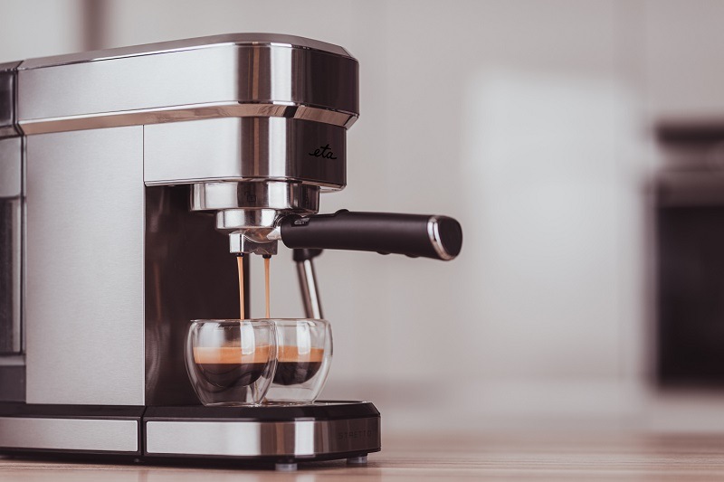 TOP 10 nejlepších dárků značky ETA Detail na nerezový pákový kávovar ETA Stretto v chodu, ze kterého proudí espresso do dvou sklenic s dvojitým dnem na dřevěné kuchyňské lince
