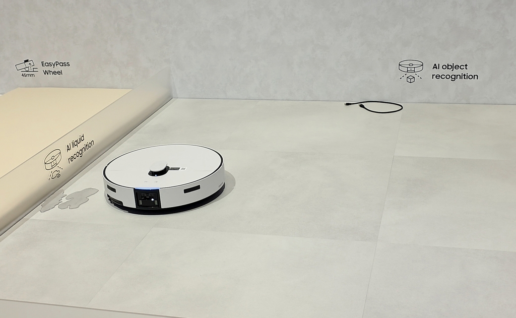 Samsung na CES 2026: AI je parťák do života Robotický vysavač Samsung Bespoke AI Jet Bot Steam Ultra vystavovaný na CES detekuje tekutinu, na pozadí je kabel pro demonstraci rozpoznání objektů