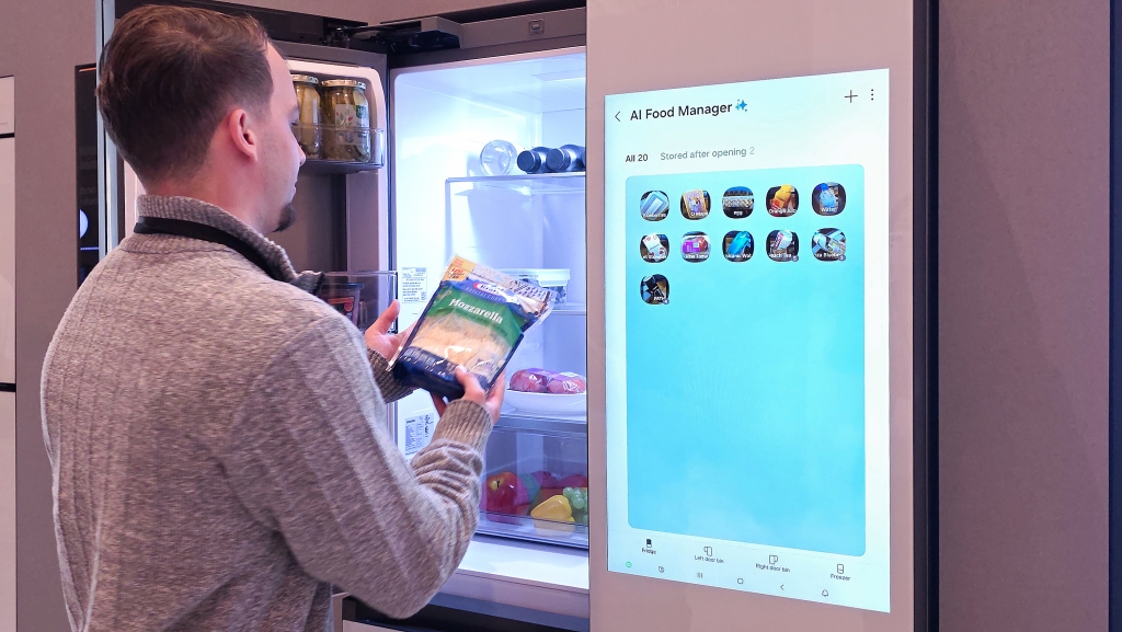Samsung na CES 2026: AI je parťák do života Muž drží v ruce sýr u otevřené lednice Samsung Family Hub vystavené na CES 2026, na displeji lednice je AI Food Manager