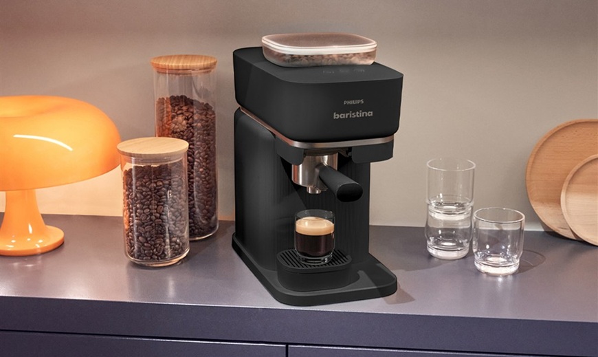 černý kávovar Philips Baristina vedle nádoby se zrnky kávy