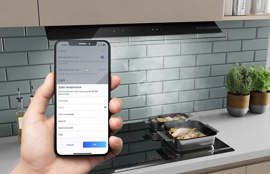 Proč si vybrat vestavnou digestoř Bosch? Náhled na mobilní telefon s aplikaci Home Connect, v pozadí varná deska a odsavač par