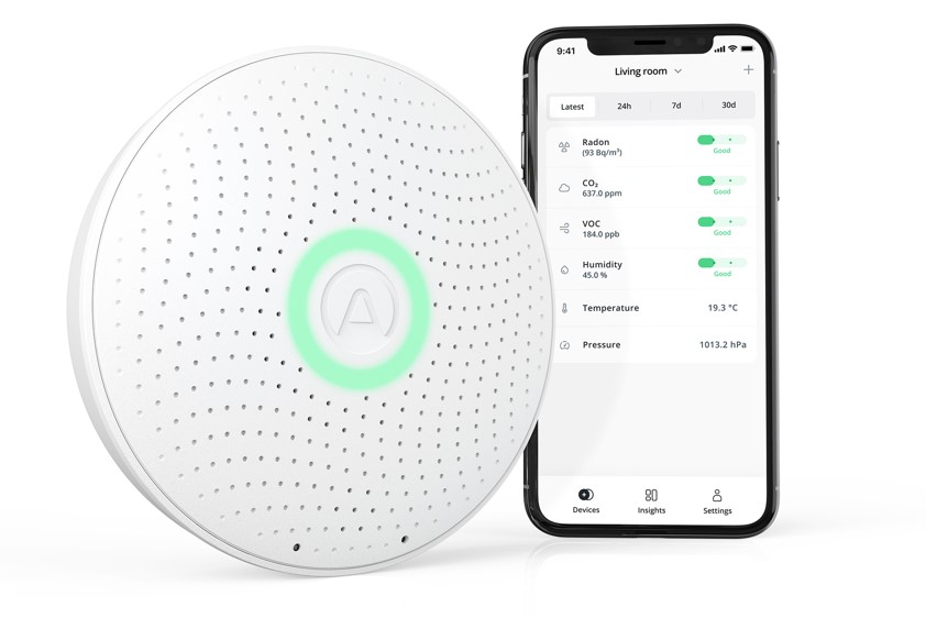 Zákeřný radon tiše ničí naše zdraví. Airthings nabízí řešení, jak ho včas odhalit kulatý senzor radonu Airthings vedle mobilu s aplikací