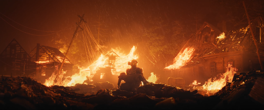 Nové Metro 2039 přijíždí: Vzhůru do podzemí! (aktualizováno) Postava Cizince drží v náruči dítě na pozadí hořících trosek, screenshot z traileru