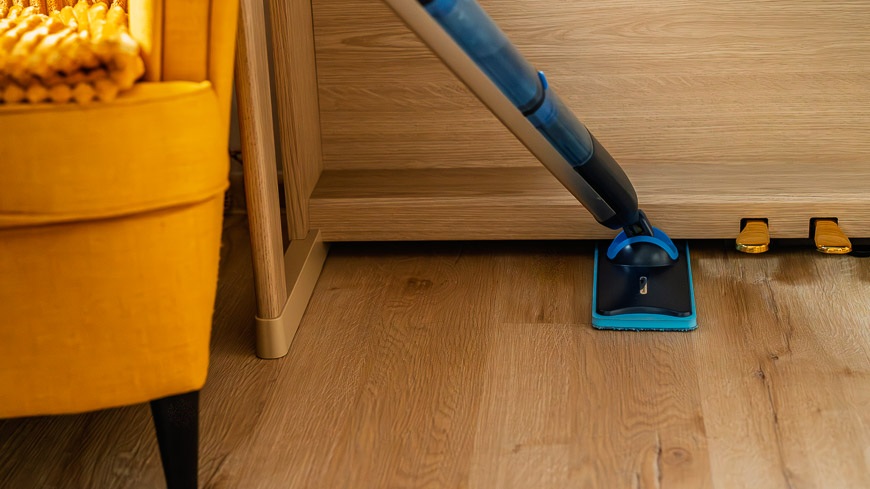 Recenze: Elektrický mop Philips OneUp – vytírejte jedním tahem a bez námahy Mop Philips OneUp zasunutý pod klavírem. V rohu část žlutého křesla.