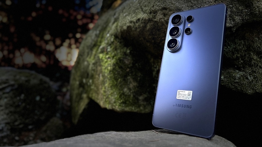 Detail zadní strany smartphonu Samsung Galaxy S26 Ultra ve fialovém provedení, opřeného o hradbu kamenů