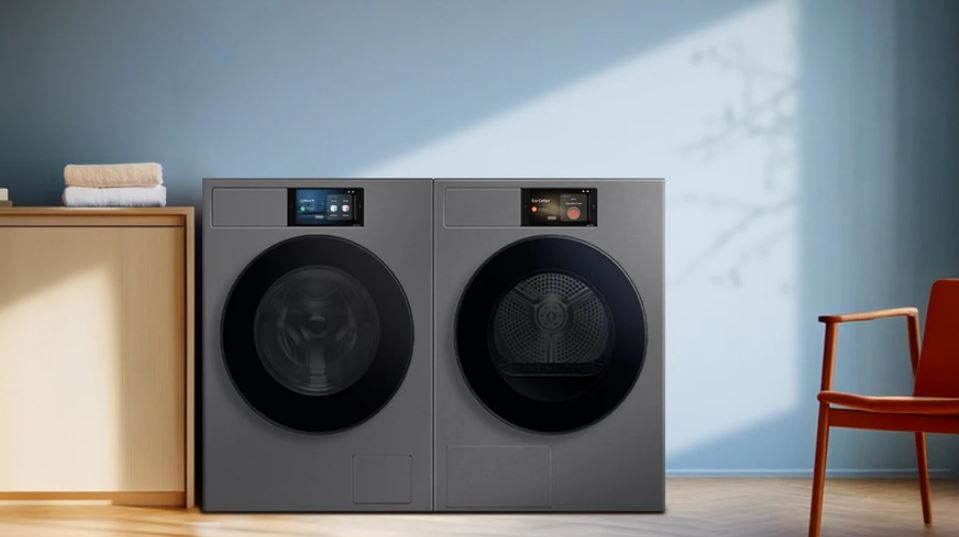 Set výrobků Samsung WF90F09C4SU4 + DV90F09F4SU4 ve stříbrné barvě a velkým ovladacím displejem. Stojí s místnosti s modrým pozadím a vedle skříně s ručníky. Na druhé straně je židle