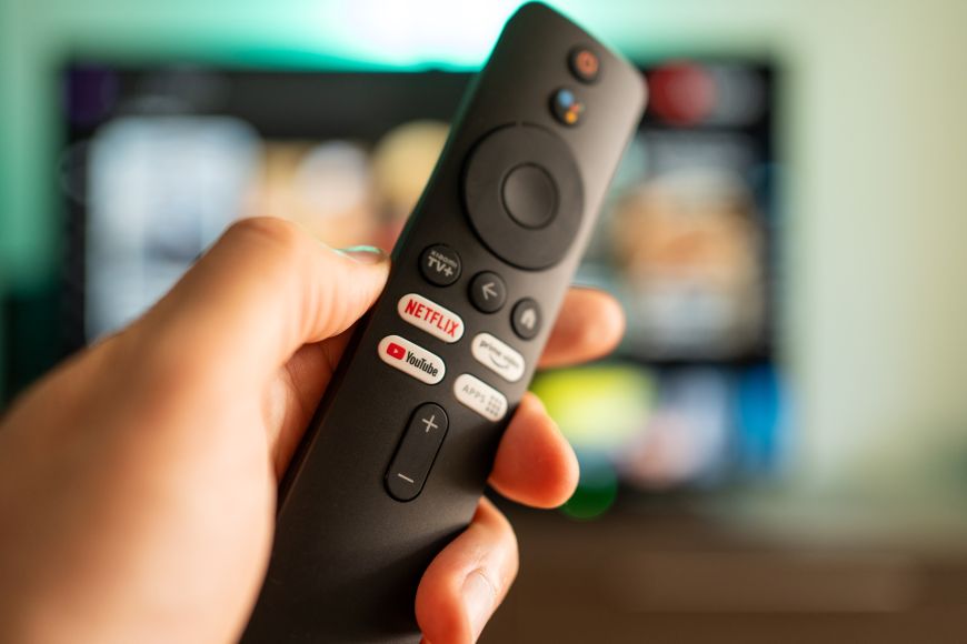 Nejčastější televizní zkratky a technologie Ukázka chytrého ovladače s televizí v pozadí