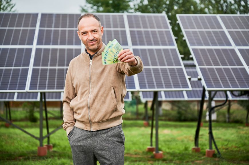 Muž s penězmi v ruce před fotovoltaickými panely