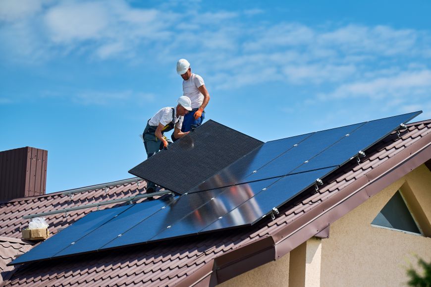 Dělníci instalují fotovoltaické panely na střechu domu za slunečného dne