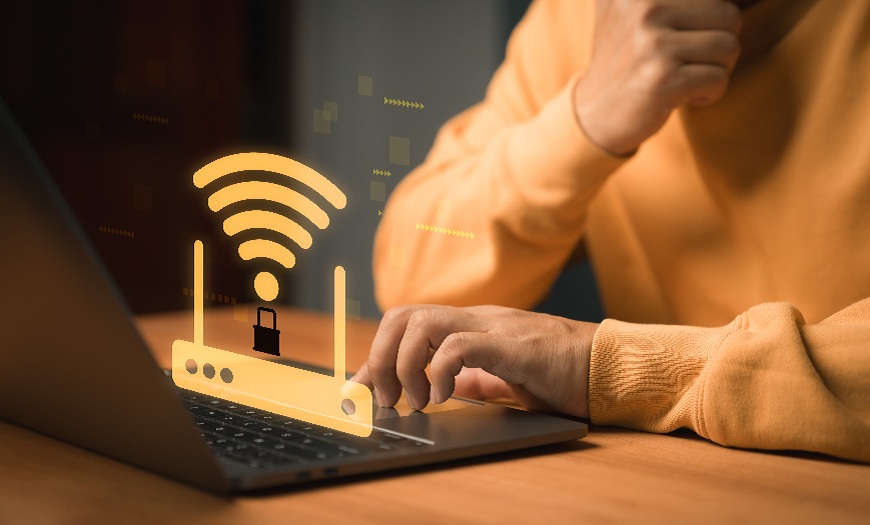 Jak nastavit rodičovskou kontrolu na chytrých zařízeních? Muž sedí u notebooku nad kterým je velký sybol Wi-Fi routeru se zámkem.