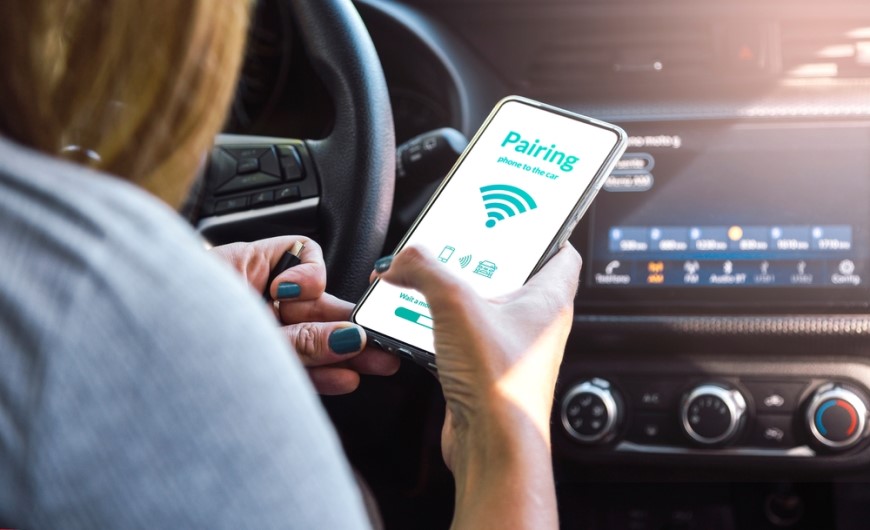 Jak spárovat telefon s autem: Průvodce, se kterým to zvládnete za 2 minuty Žena sedí v autě na místě řidiče a snaží se spárovat telefon s autem