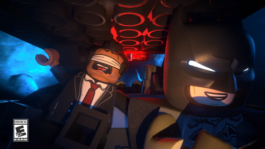 LEGO Batman řídí vozidlo a směje se, za ním sedí postava se zavázanýma očima