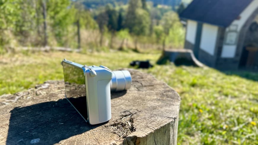 Boční pohled na smartphone vivo X300 Ultra s nasazeným Imaging Gripem, položený na pařezu v terénu. 