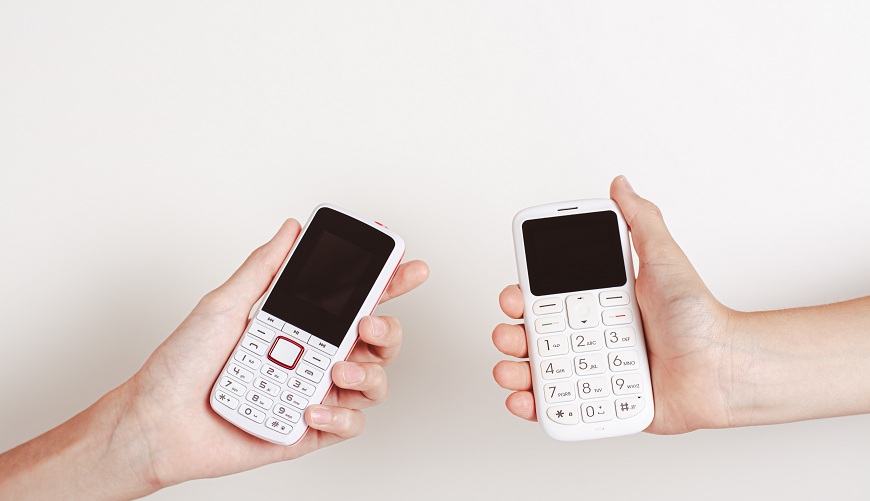Dva bílé mobilní telefony s tlačítky v rukou. 