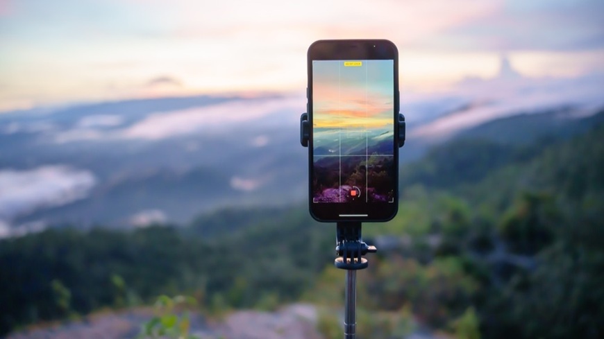 Jak pořídit dobré fotky mobilem? Mobilní telefon, usazený na stativu, při fotografování večerní krajiny v pozadí