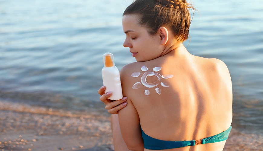 Mladá žena sedící na pláži s SPF krémem