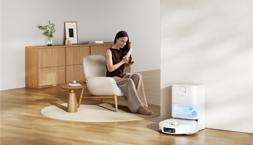Žena si upravuje vlasy, zatímco robotický vysavač Xiaomi Robot Vacuum H50 Pro se v dokovací stanicí dobíjí
