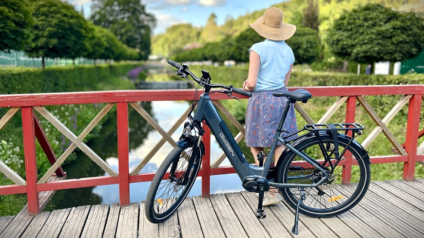 Recenze: Elektrokolo GoGEN Aspen MX 720 se postará o to, aby vaše cyklochoutky nic nebrzdilo Elektrokolo GoGEN Aspen MX 720 stojící na mostě před ženou v apartním klobouku, která pozoruje tekoucí říčku v pozadí