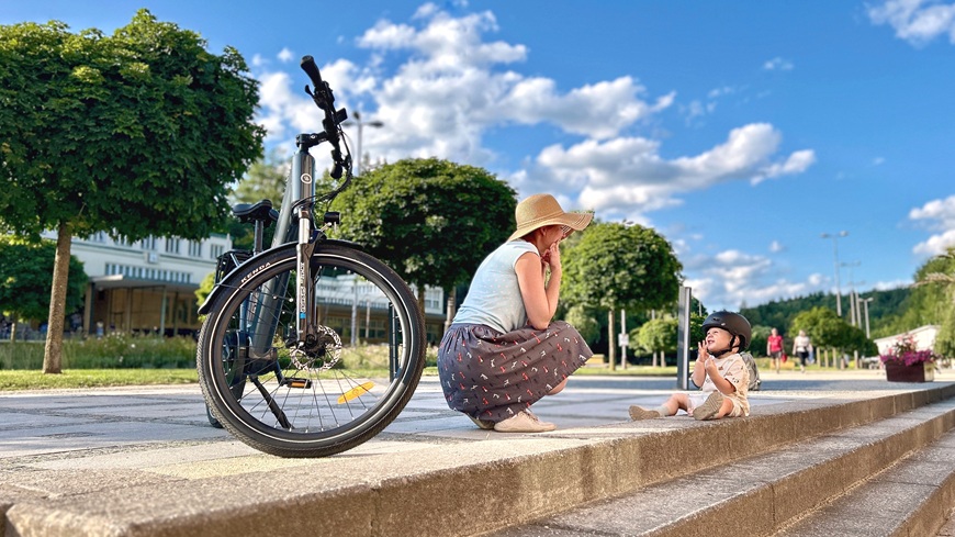 Recenze: Elektrokolo GoGEN Aspen MX 720 se postará o to, aby vaše cyklochoutky nic nebrzdilo Elektrokolo GoGEN Aspen MX 720 v šedo-černém provedení, opřené o stojan, na pozadí žena s batoletem
