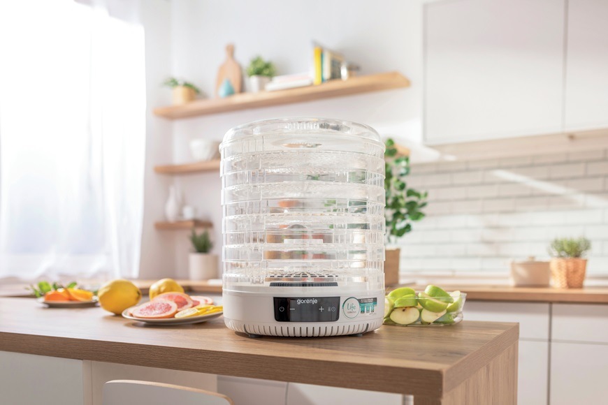 Nejlepší pomocníci na léto? Vychytávky Gorenje pro prázdninovou pohodu pruhledná sušička ovoce gorenje na kuchynské lince v dřevěnem dekoru. Je prázdná a vedle ni lezi připravene ovoce