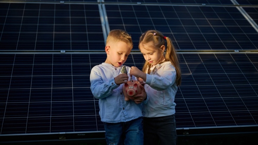 Jak na fotovoltaiku v roce 2026: Získejte solární elektrárnu bez úroků a počátečních úspor! Chlapec a dívka s prasátkem, do něhož vkládají úspory na fotovoltaiku v pozadí