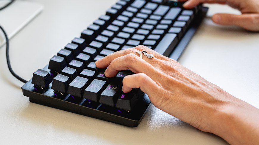 Herní klávesnice Razer Huntsman Tenkeyless V3 8KHz s fialovým podsvícením leží na stole, na klávesnici jsou položené ruce, pohled z boku
