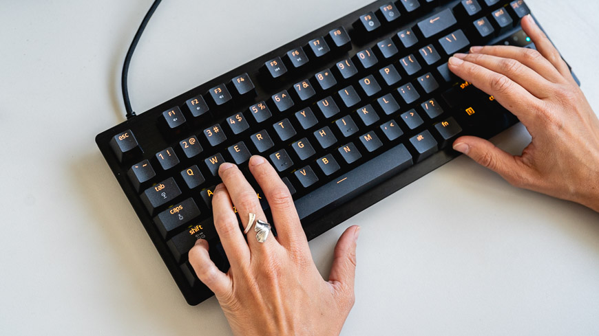 Herní klávesnice Razer Huntsman Tenkeyless V3 8KHz s oranžovým podsvícením leží na stole, na klávesnici jsou položené ruce