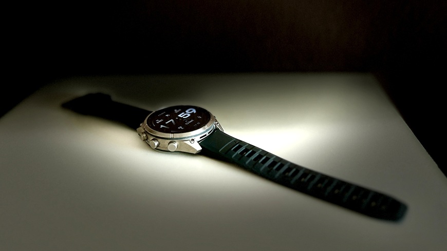 Chytré hodinky Garmin fēnix® 9 Pro v detailu s krabičkou na spoře osvětlené poličce