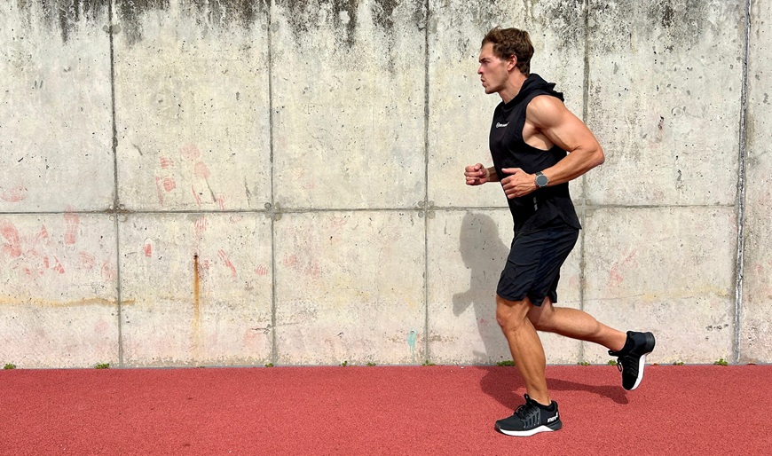 Muž ve sportovním outfitu běžící po atletické dráze s chytrými hodinkami Garmin fēnix® 9 Pro na zápěstí