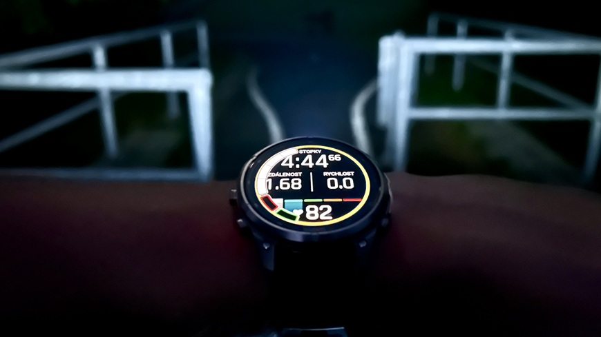 Chytré hodinky Garmin fēnix® 9 Pro osvětlují výkonnou svítilnou potemněnou noční cyklostezku s průjezdovým mostem v pozadí