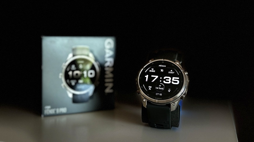 Chytré hodinky Garmin fēnix® 9 Pro v detailu s krabičkou na spoře osvětlené poličce