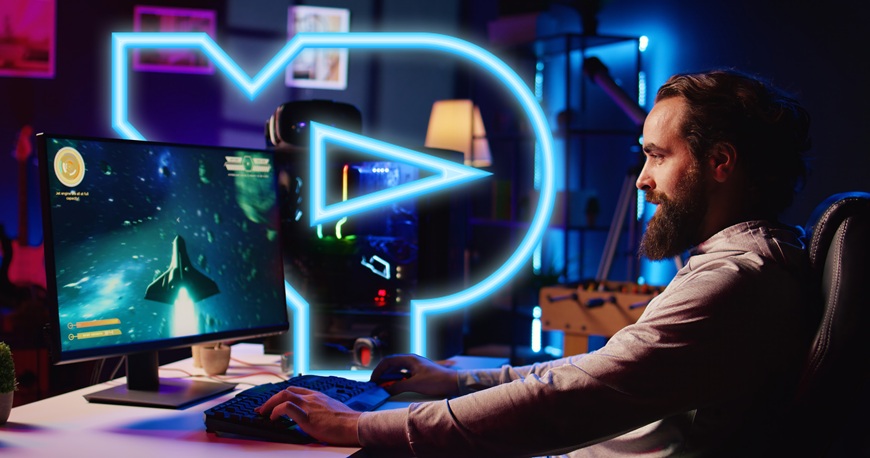 Muž sedí u stolu a hraje hru na PC, na pozadí je svítící neonové logo DATART XP