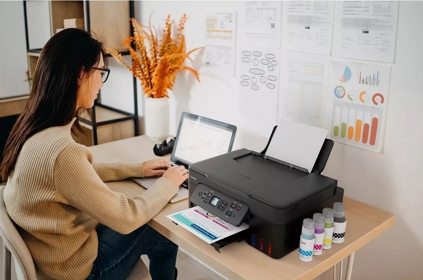 Jak vybrat tiskárnu? Žena pracuje na notebooku. Vedle sebe na stole má tiskárnu Canon PIXMA G3480.