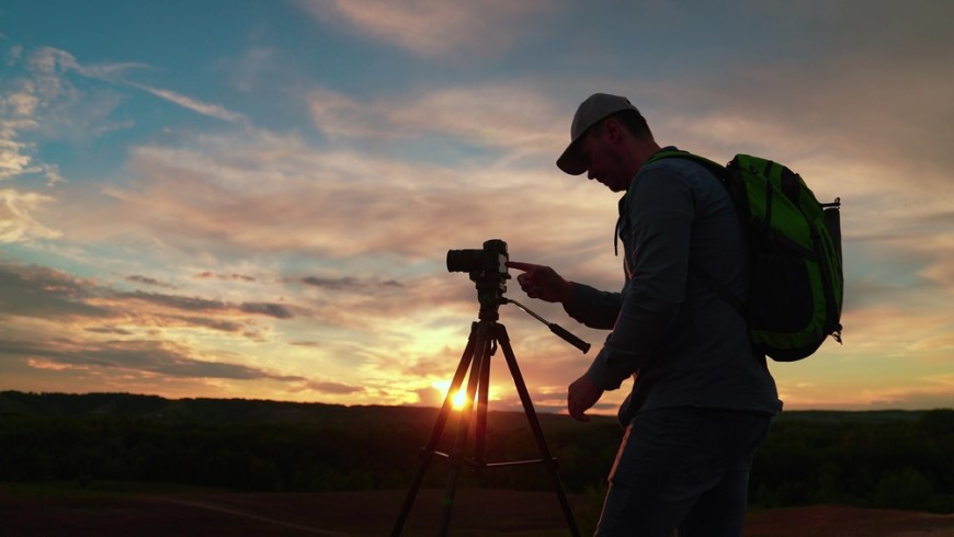 Muž fotografuje západ slunce digitálním fotoaparátem na stativu