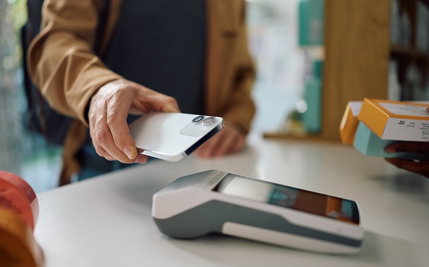 Jak platit mobilním telefonem? Muž přikládá mobilní telefon k platebnímu terminálu.