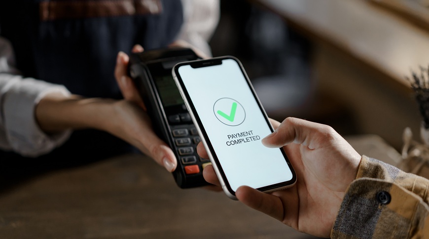 Jak platit mobilním telefonem? Muž přikládá mobil k terminálu a na displeji svítí oznámení o schválení platby.